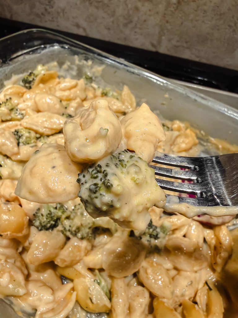 Creamy no-boil broccoli pasta bake with shells and cheese sauce on a fork, fresh from the baking dish